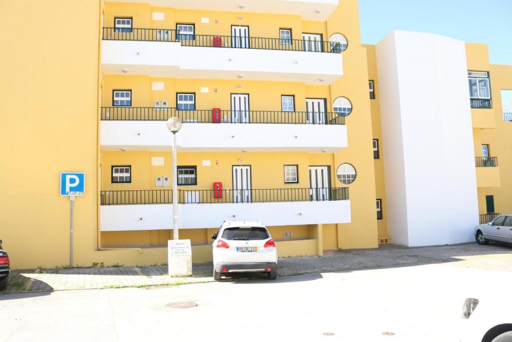 biały samochód zaparkowany przed żółtym budynkiem w obiekcie Apartamento Maria w Alvor