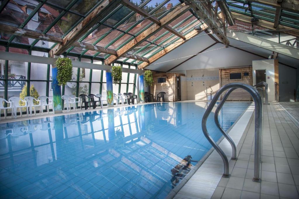 Indoor pool under glass roof with poolside chairs and metal ladder, bright reflections