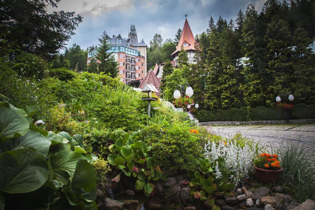 Lush garden beds and lamp posts leading toward a turreted hotel partially hidden by trees.