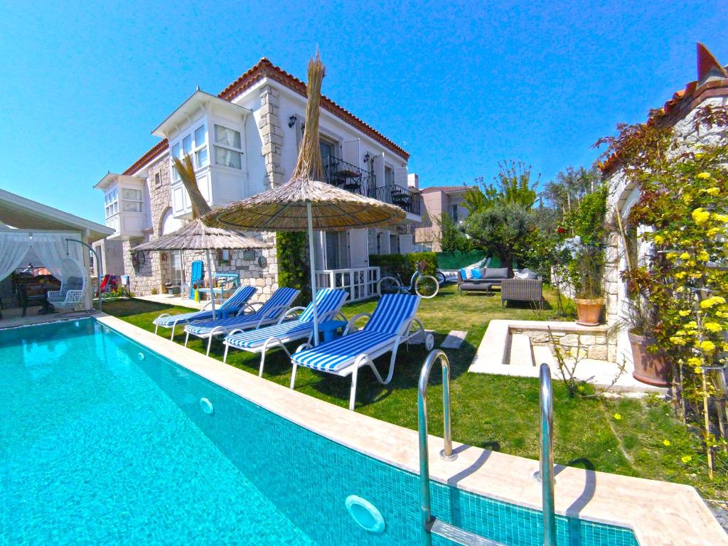 a swimming pool with chairs and an umbrella next to a house at Morisi Konak Butik Otel in Alacati