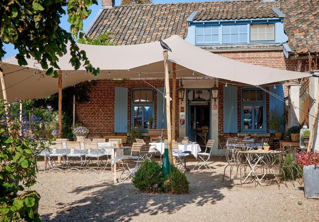 un patio con mesas y sillas bajo una sombrilla blanca en Gasterie Lieve Hemel, en Sevenum