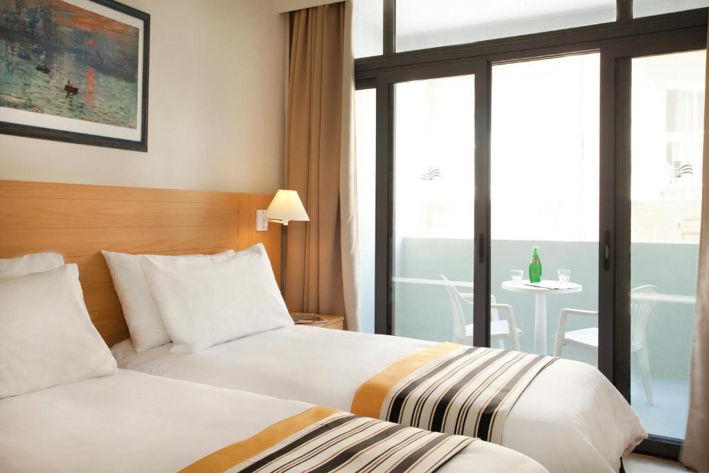 two beds in a hotel room with a view of a table at The Preluna Hotel in Sliema
