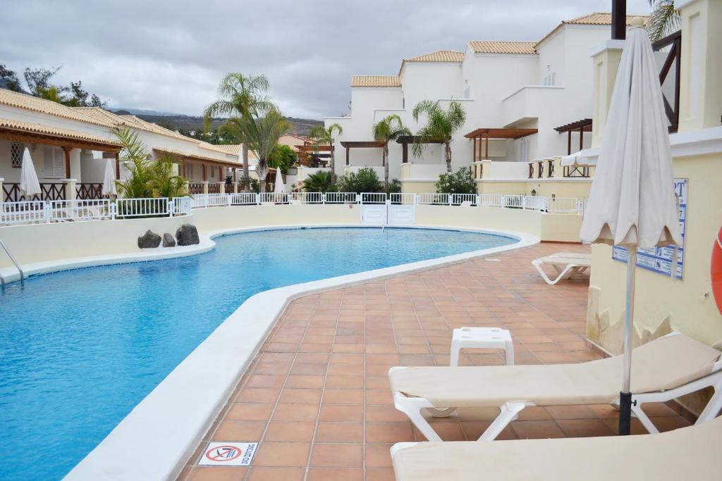 a pool with chairs and umbrellas next to a building at Golf Resort Tenerife sur in Los Cristianos