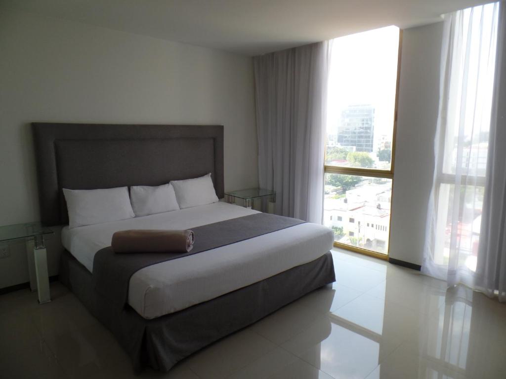 Cama en habitación de hotel con ventana grande en Hotel Suites Bernini en Guadalajara