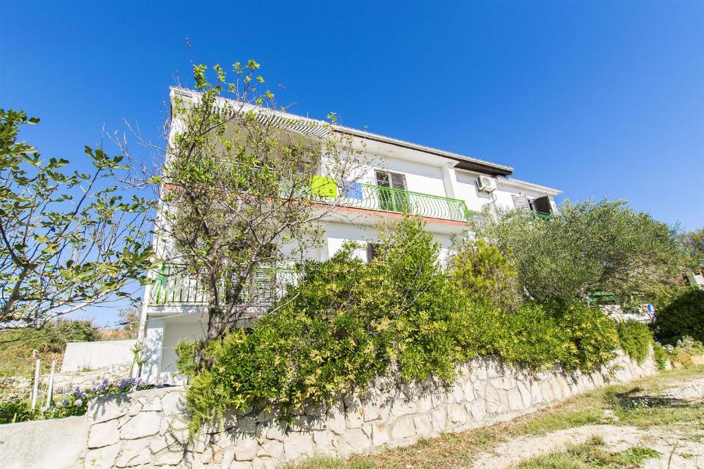 a white house on a stone wall with bushes at Apartments Milena in Rtina