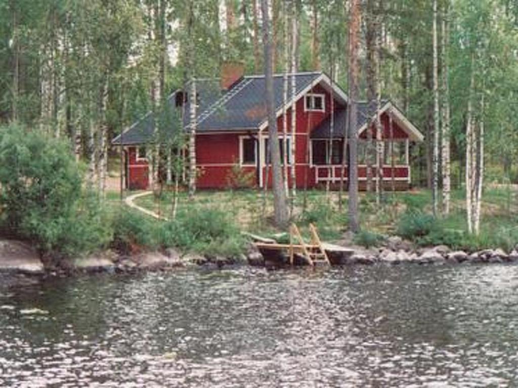 une cabine rouge dans les bois à côté d'une nappe d'eau dans l'établissement Holiday Home 6332 by Interhome, à Rantakylä