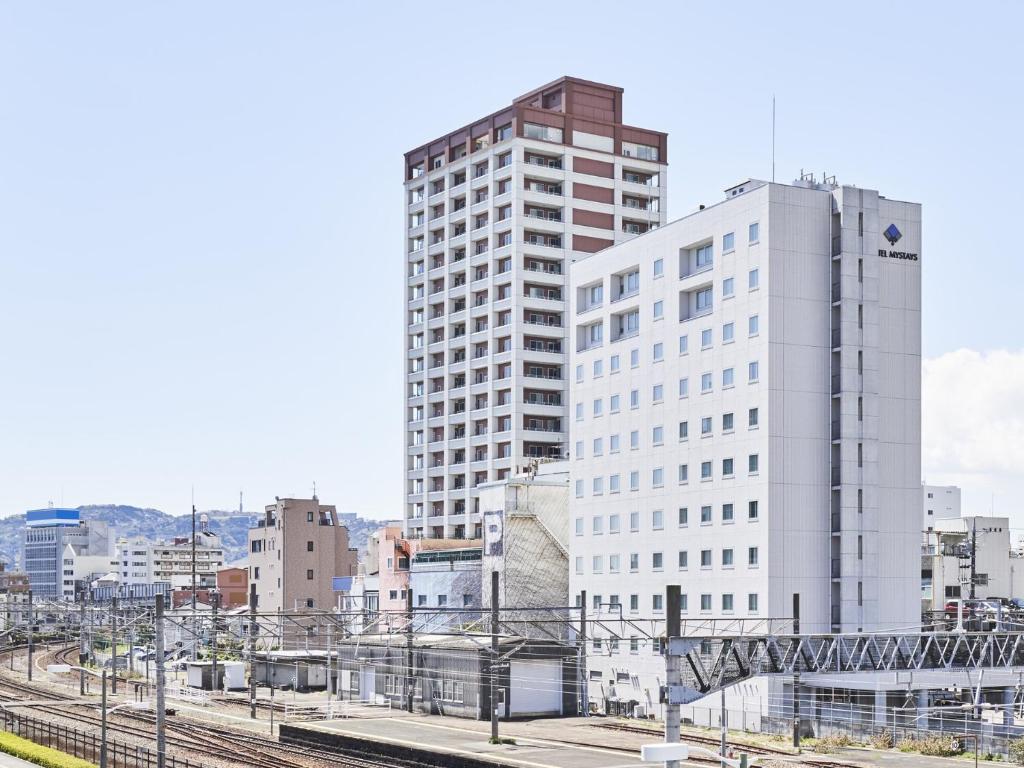 a tall white building next to a train station at HOTEL MYSTAYS Shimizu in Shizuoka