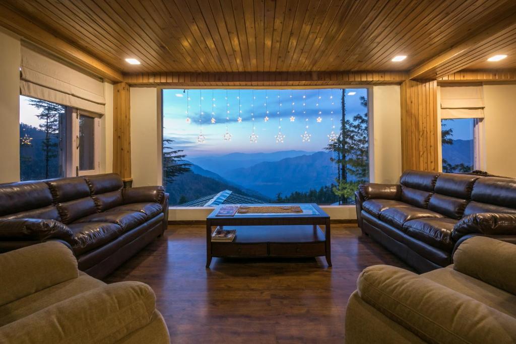 a living room with leather couches and a large window at StayVista at The Corner House - Pet Friendly Villa in Shimla
