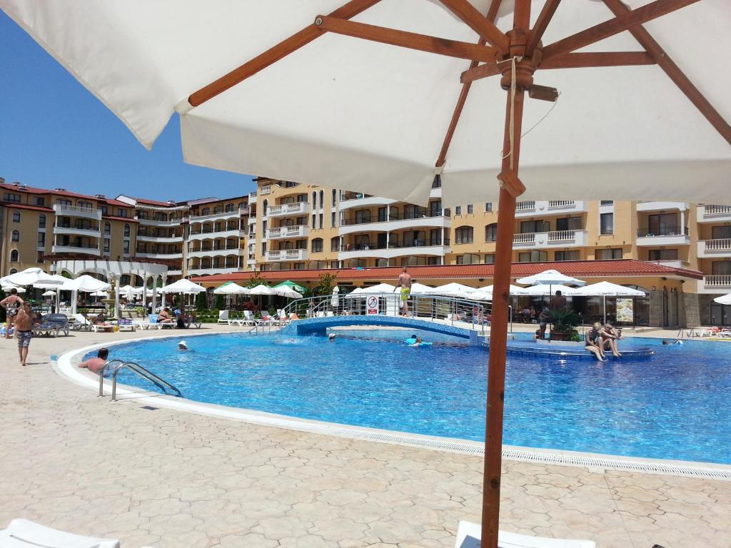 a swimming pool with an umbrella and some buildings at Menada Royal Sun Apartments in Sunny Beach