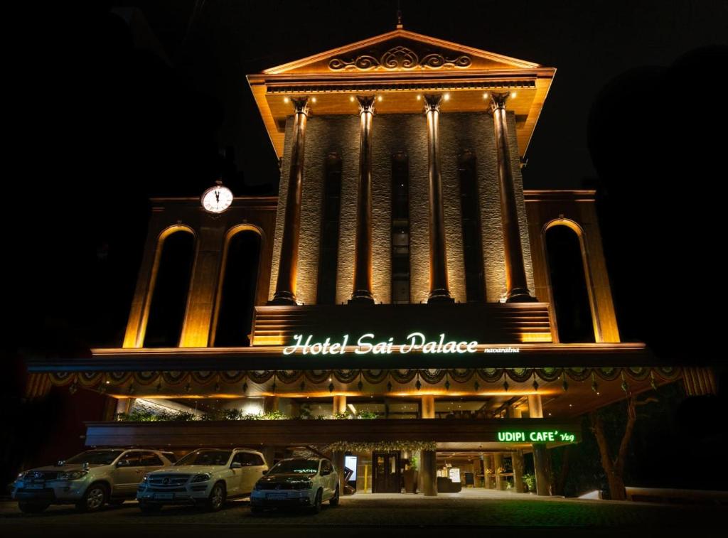 un bâtiment avec une tour d'horloge avec des voitures garées devant dans l'établissement Hotel Sai Palace , Mangalore, à Mangalore