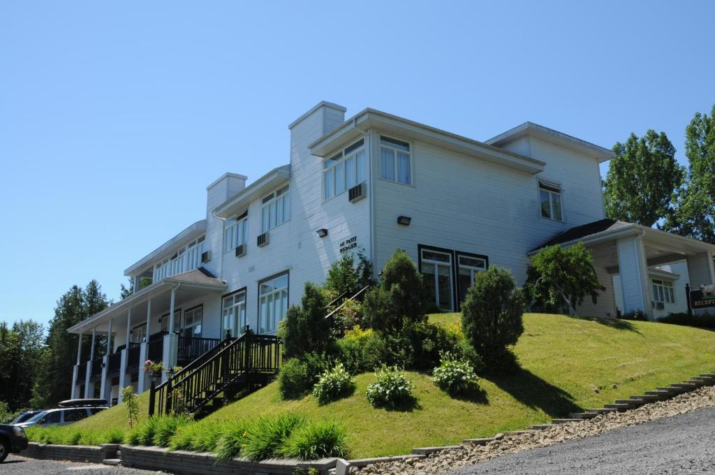 un grand bâtiment blanc sur une colline avec des buissons dans l'établissement Hôtel au Petit Berger, à La Malbaie