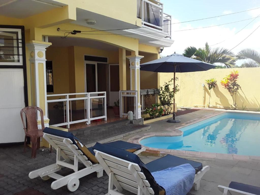 a house with a swimming pool with chairs and an umbrella at La villa de christiane in Grand Baie