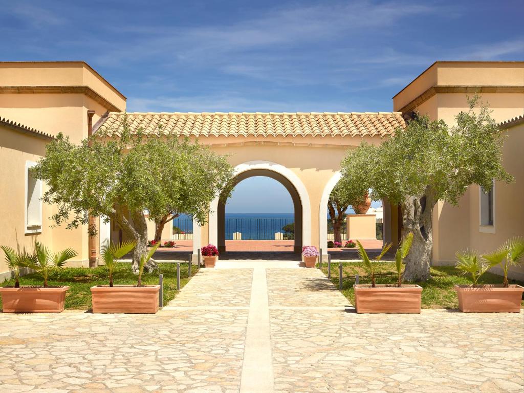 a building with an arch and trees in a courtyard at Hapimag Resort Cefalù in Cefalù