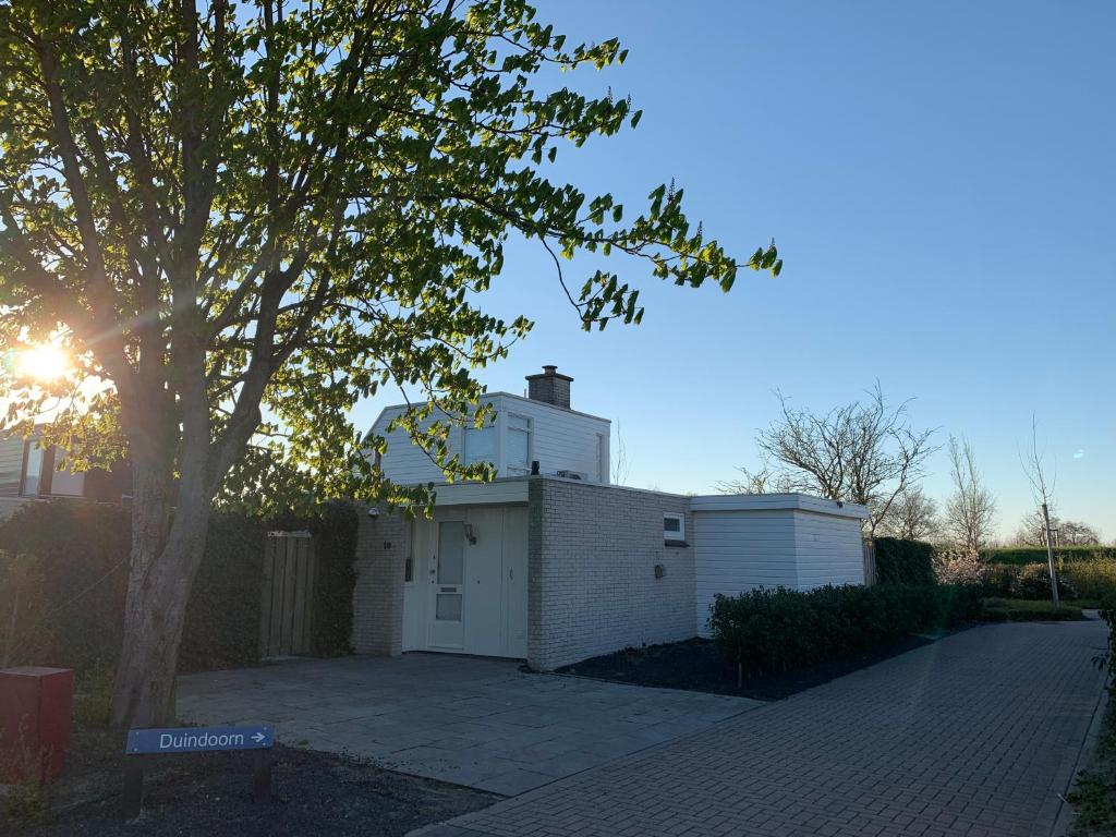 a white house with a tree in front of it at Vakantiebungalow Mee naar Ouddorp aan zee in Ouddorp