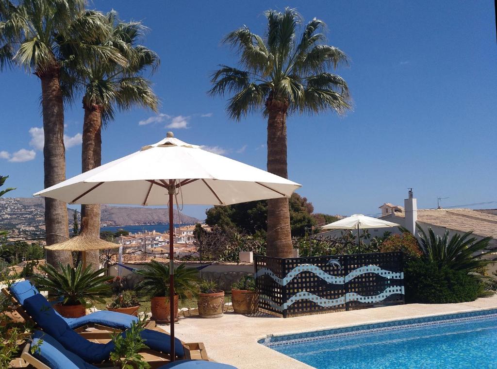 a pool with chairs and an umbrella and palm trees at Villa Las Palmeras with private pool and garden in Altea