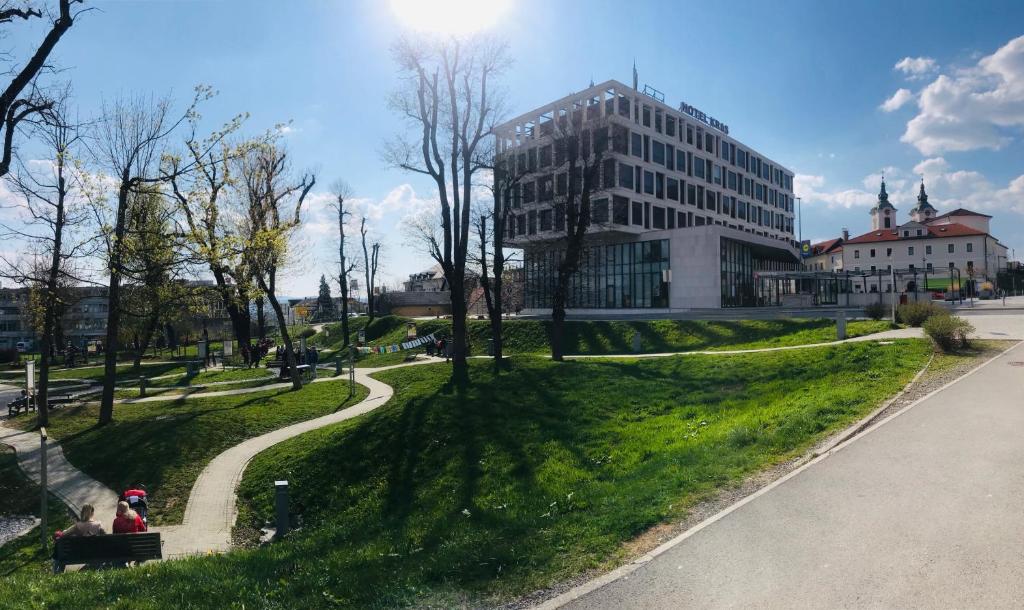 eine Person, die auf einer Bank in einem Park mit einem Gebäude sitzt in der Unterkunft Hotel Kras in Postojna