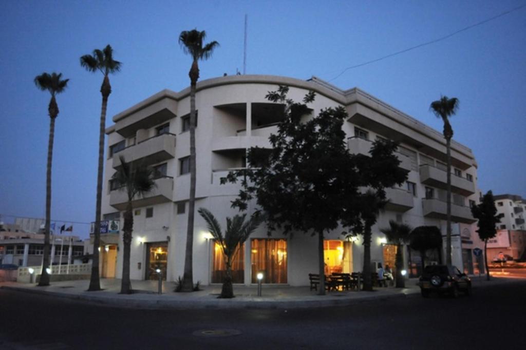 a large white building with palm trees in front of it at Elysso Hotel in Larnaca