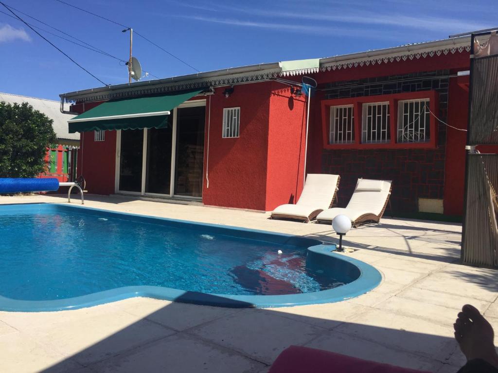 a swimming pool in front of a red building at VyvyRUN974 in Les Cocos