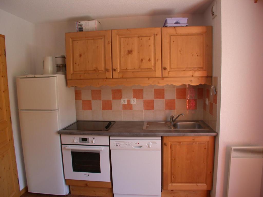 a kitchen with wooden cabinets and a sink and a refrigerator at L&#39;Ecrin des Neiges in Vars