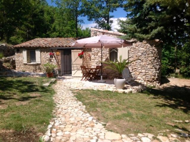 ein kleines Steinhaus mit einem Tisch und einem Sonnenschirm in der Unterkunft Le bastidon du Luberon in Caseneuve