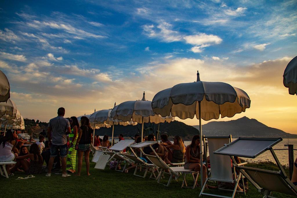 a group of people sitting in chairs under umbrellas at Maresia Rooms in Procida