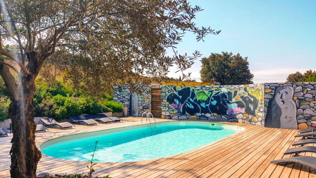 a swimming pool with a wooden deck and a wall with graffiti at Hôtel Ascosa Aventure in Ponte-Leccia