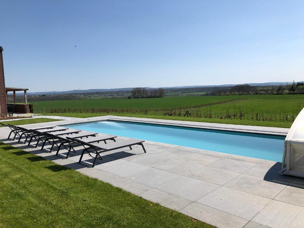 a swimming pool with benches next to a field at Vue d'en Haut in Durbuy