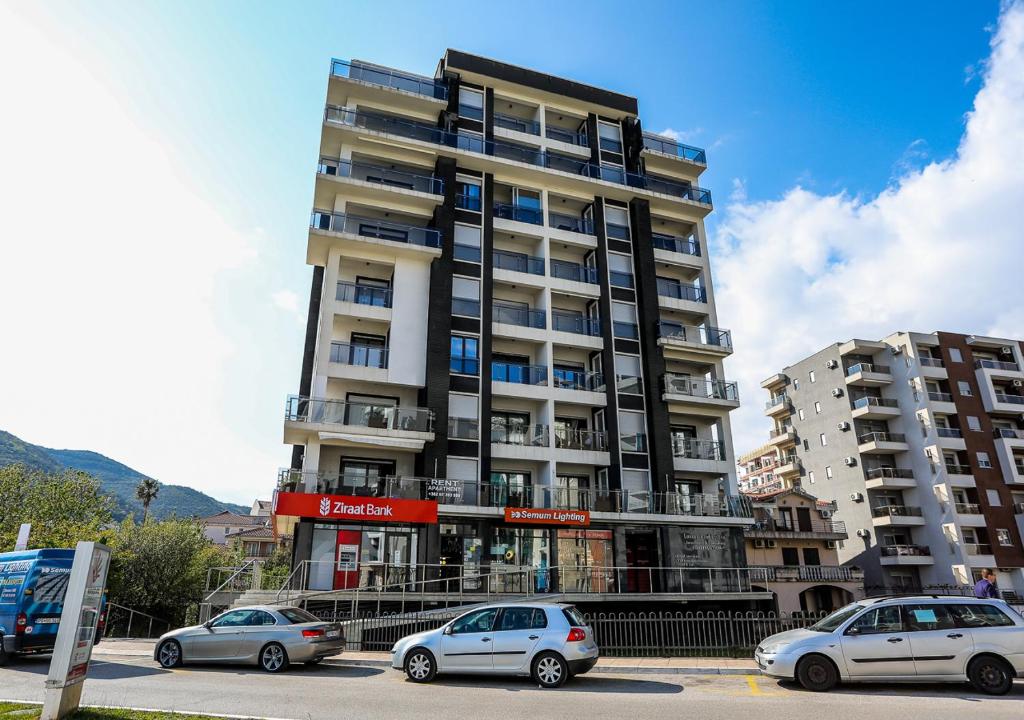 Un grand bâtiment avec des voitures garées devant lui dans l'établissement Budva Bay Breeze Apartments, à Budva