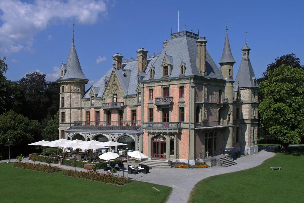um castelo com mesas e guarda-chuvas à sua frente em Schloss Schadau - Swiss Historic Hotel em Thun
