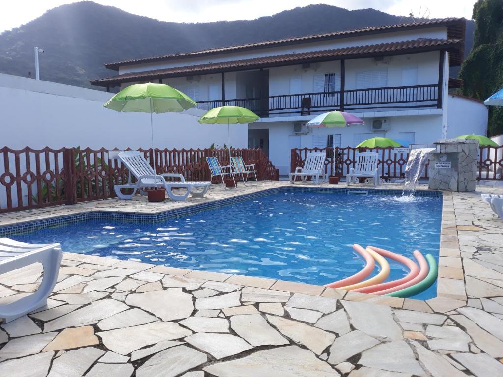 a pool with chairs and umbrellas next to a house at POUSADA TANI COM AR E PISCINA em MARESIAS in Maresias