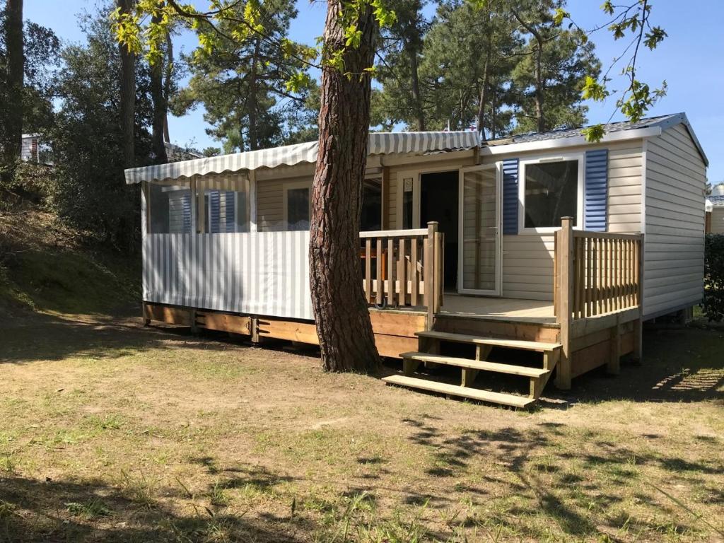 une petite maison avec une véranda et un arbre dans l'établissement Mobile Home - Camping, aux Mathes