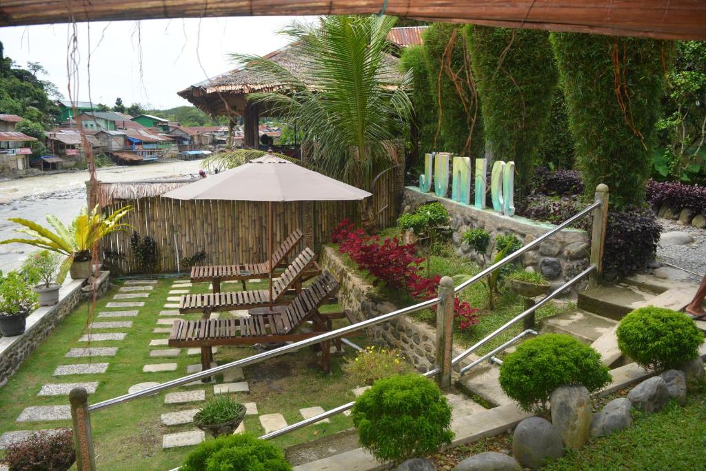 a garden with chairs and an umbrella and surfboards at Junia Guesthouse Bukit Lawang in Bukit Lawang