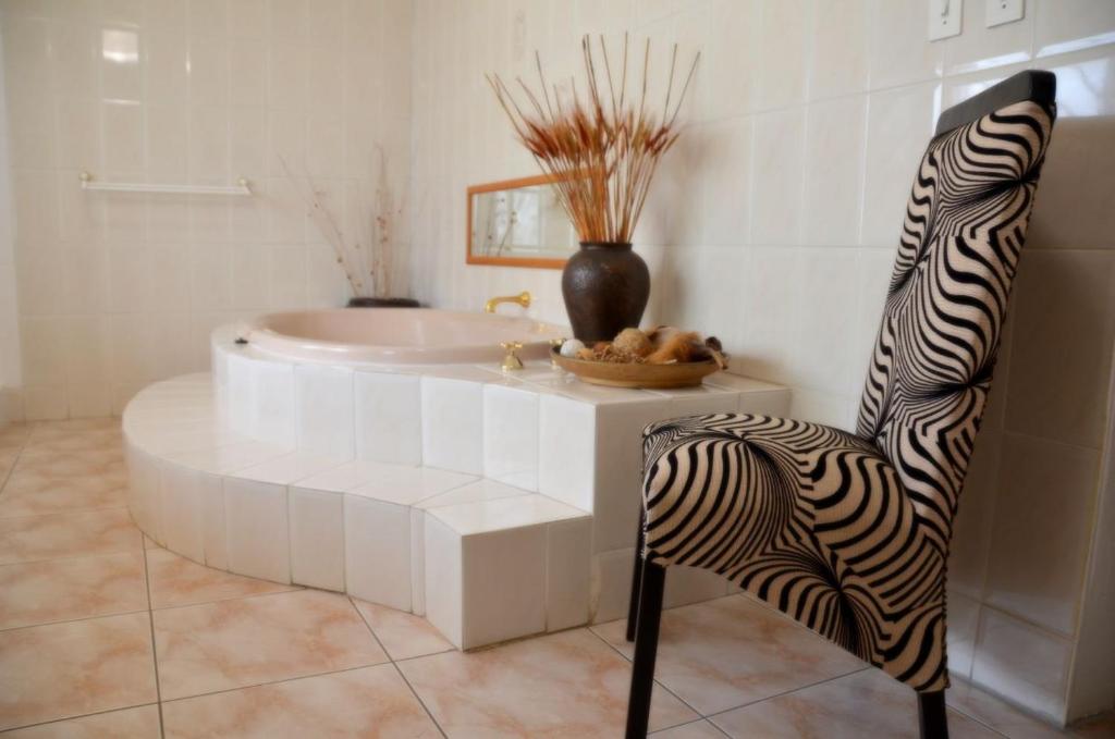 La salle de bains est pourvue d'une baignoire et d'un fauteuil zèbre. dans l'établissement Azrielle Guesthouse, à Sasolburg