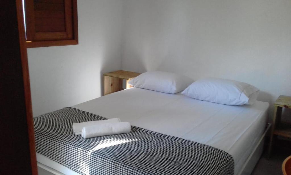 Una cama blanca con dos almohadas encima. en Mandacaru Guest House, en Praia do Forte