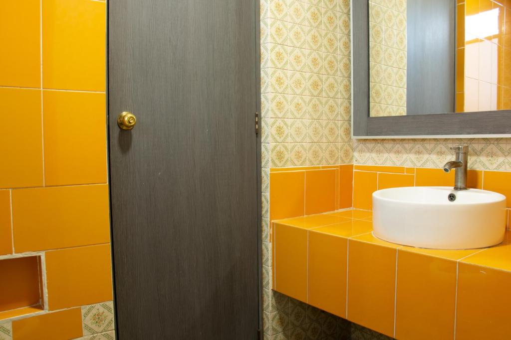 A compact bathroom vanity has a white vessel sink against vivid orange and patterned tile.