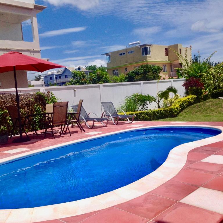 a swimming pool with chairs and an umbrella and a house at Cardamon Villa is a 2 bedroom with 1 bathroom and seperate toilet detached house with AC and swimming pool , 5 minutes walk from Flic en Flac public beach in Flic-en-Flac