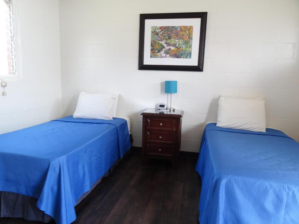 two beds in a room with blue sheets and a nightstand at Tip Top Motel in Lihue