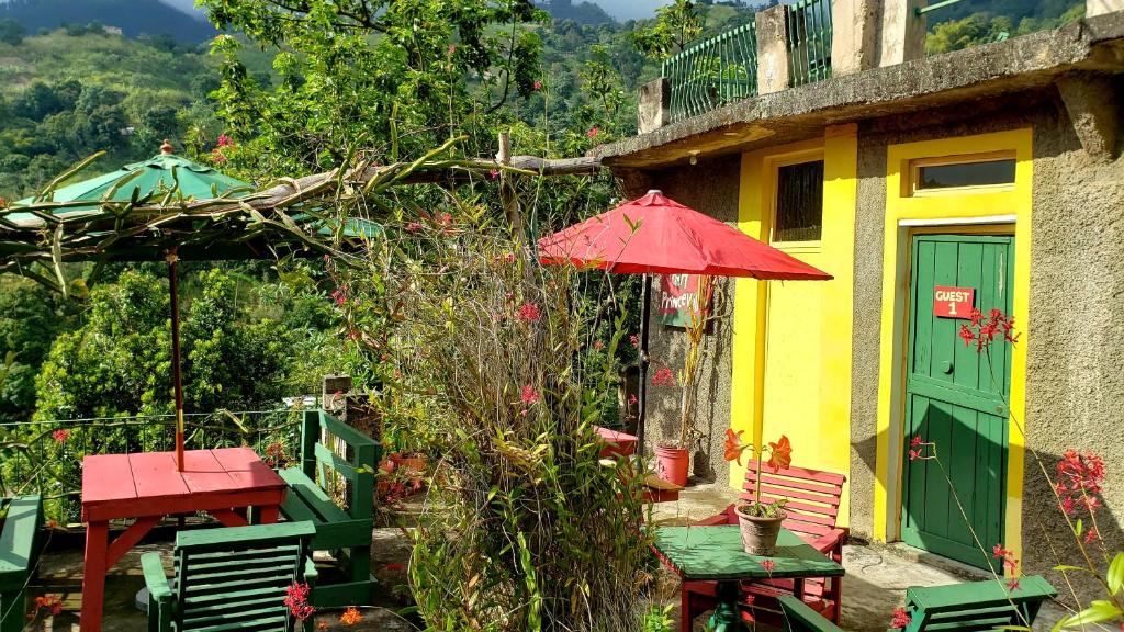 uma casa com um guarda-sol vermelho, uma mesa e cadeiras em Prince Valley Guesthouse em Irish Town