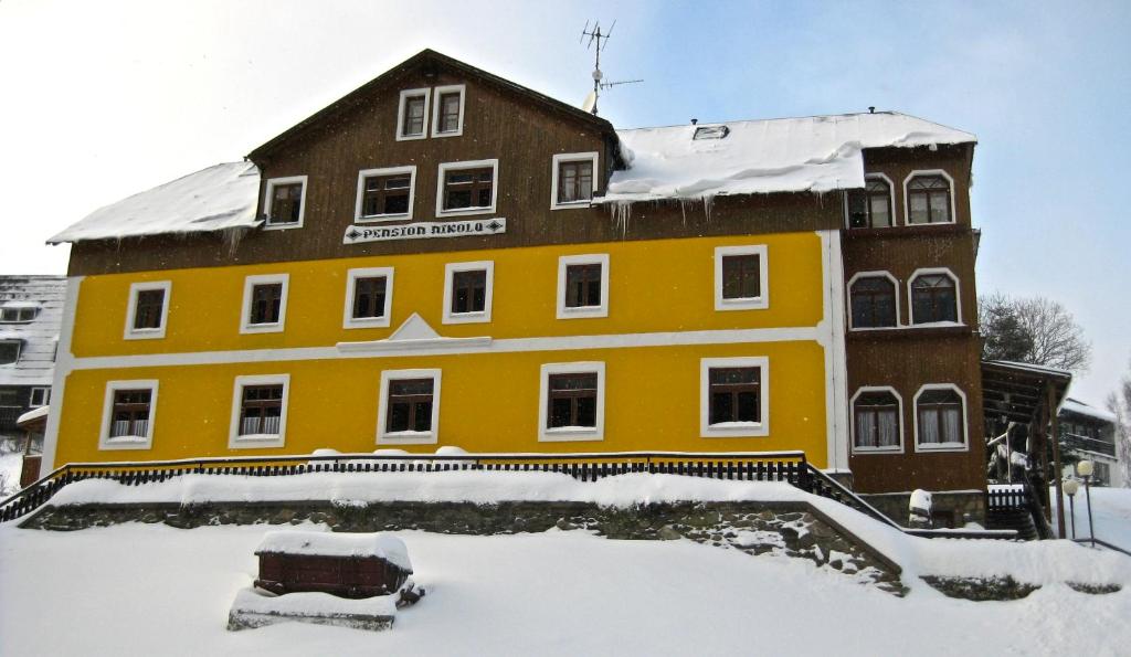 a yellow building in the snow with a car in front at Penzion Nikola in Pec pod Sněžkou