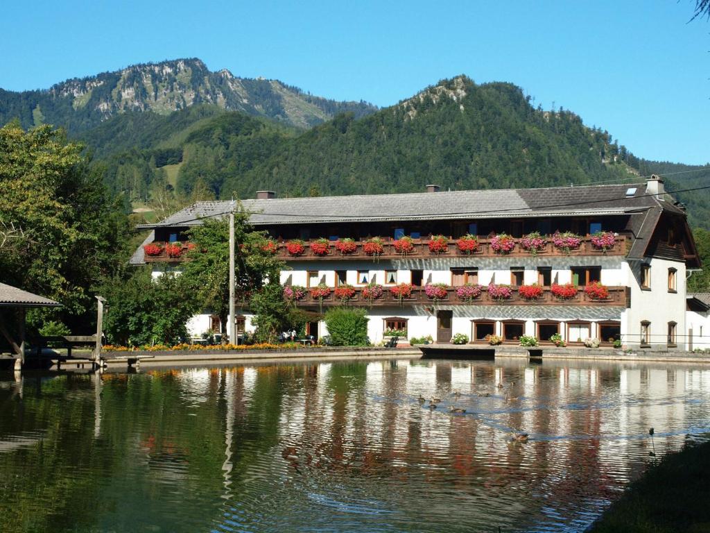 a building next to a lake in front of a mountain at Wieselmühle Forellenhof in Grünau im Almtal