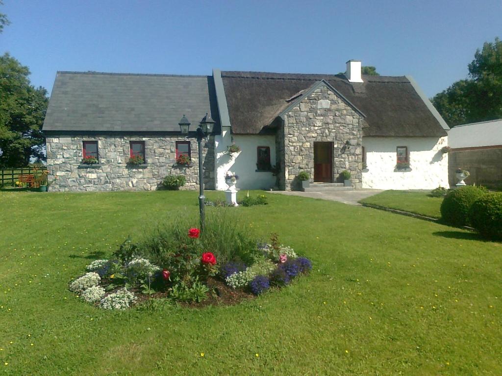 una casa de piedra con flores frente a un patio en The Thatched Cottage B&B, en Claregalway