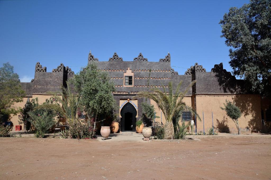 an old building with a gate and trees in front of it at Haven La Chance Desert Hotel in Merzouga