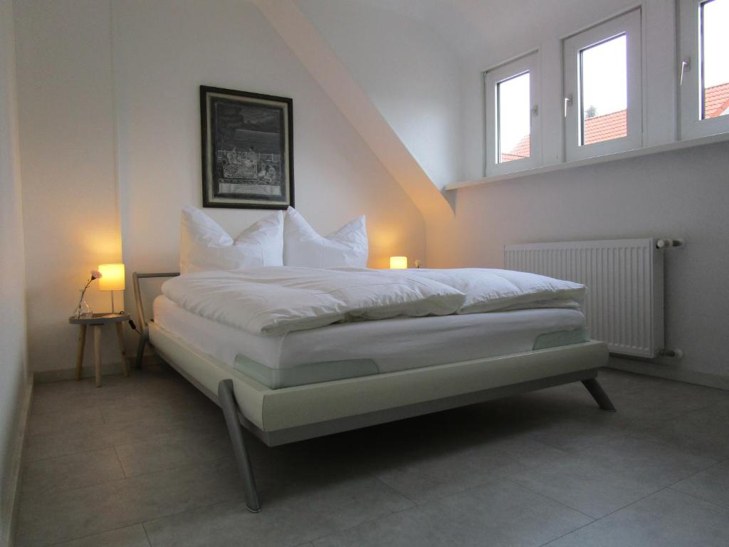 una camera da letto con un letto con lenzuola bianche e due finestre di Schicke Komfortwohnung zum Wohlfühlen a Merchweiler