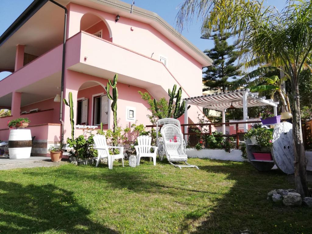 uma casa rosa com cadeiras brancas no quintal em La Gramigna Villette em Briatico