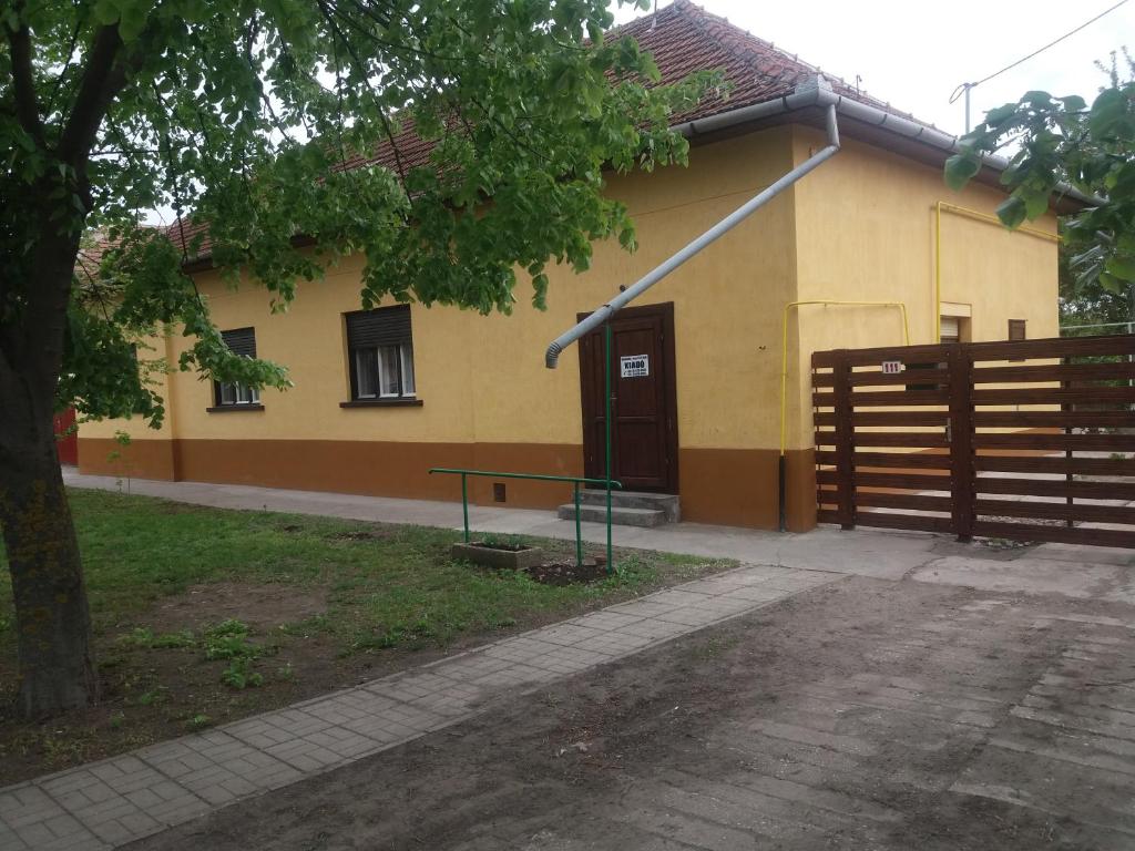 una casa amarilla con una valla y un banco delante de ella en Hársfák en Mezőkovácsháza
