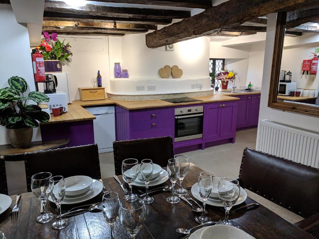 a kitchen with purple cabinets and a table with wine glasses at Cotswolds Valleys Accommodation - Medieval Hall - Exclusive use character three bedroom holiday apartment in Stroud