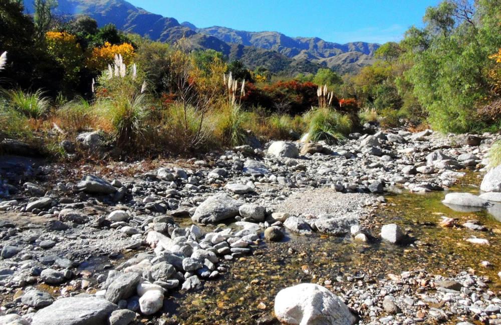 a rocky river with rocks and trees and mountains at ASM CABAÑAS XIII in Merlo
