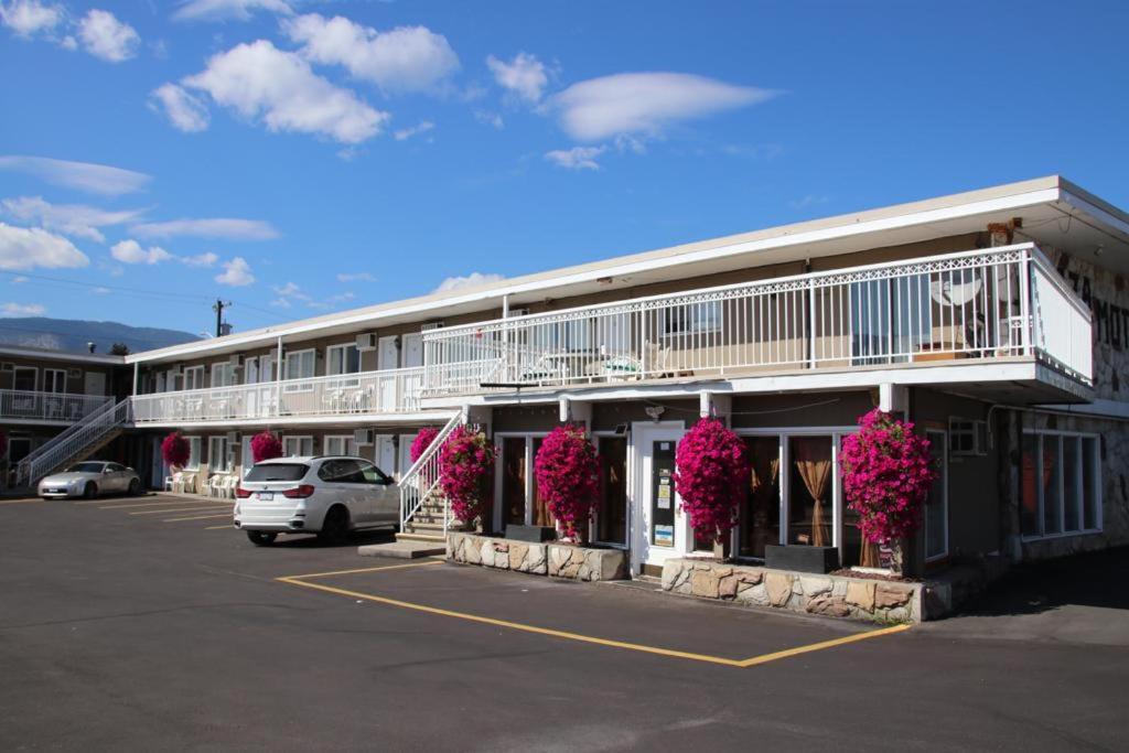 un bâtiment avec des fleurs roses dans un parking dans l'établissement Plaza Motel, à Penticton