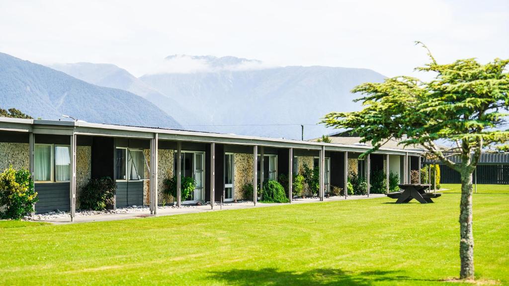 ein Haus mit einem grünen Hof mit Bergen im Hintergrund in der Unterkunft Heartland Hotel Haast in Haast