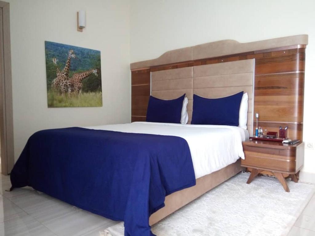 um quarto com uma cama grande com lençóis azuis e uma pintura de girafa em Ikaze B&B em Kigali